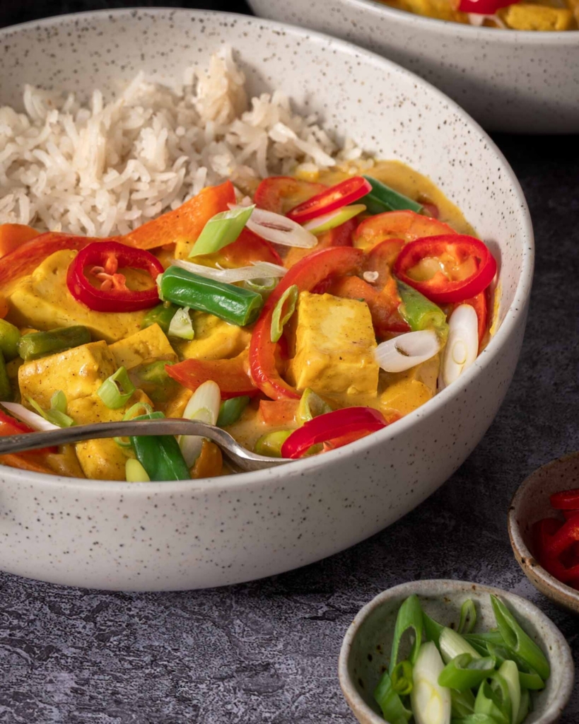 A close up image of a bowl of vegan Chinese curry, topped with fresh chilli and spring onion