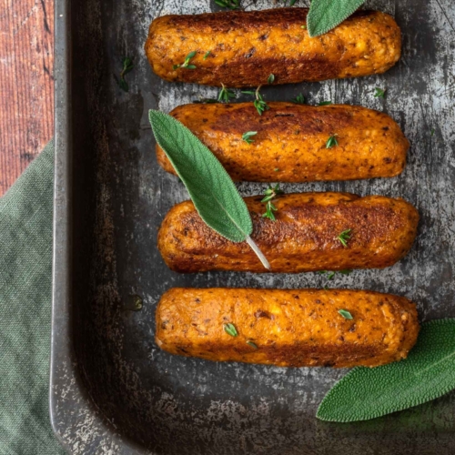 An oven tray filled with golden, crispy vegan tofu sausages