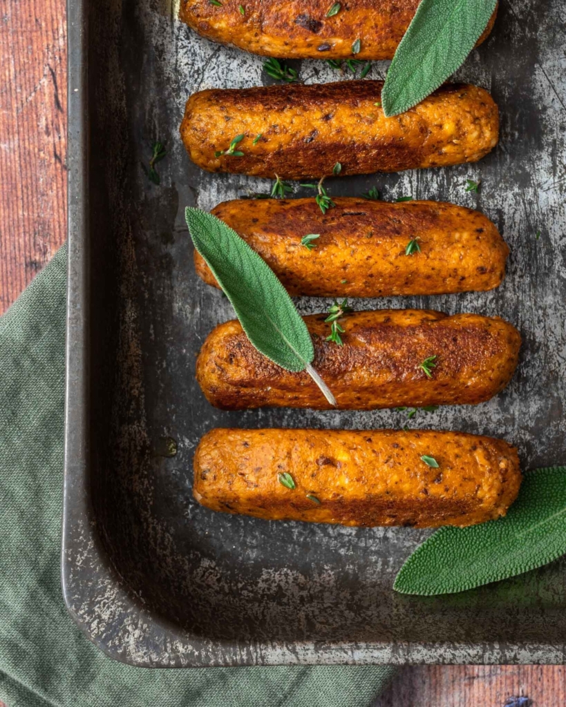 An oven tray filled with golden, crispy vegan tofu sausages