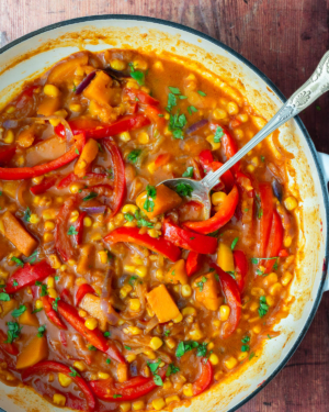 A colourful sweet corn curry with butternut squash and red pepper, being cooked in a cast iron pan