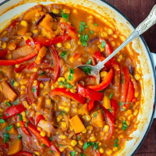 A colourful sweet corn curry with butternut squash and red pepper, being cooked in a cast iron pan