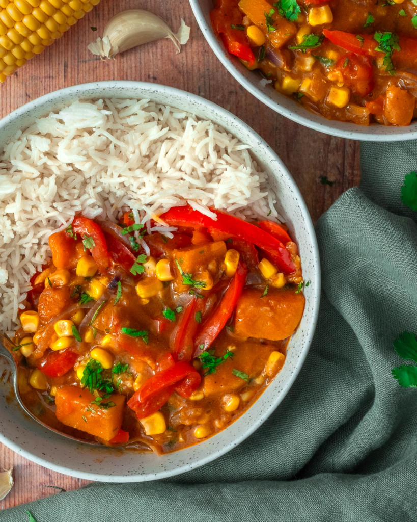 A colourful sweet corn, squash and red pepper curry in a bowl with rice