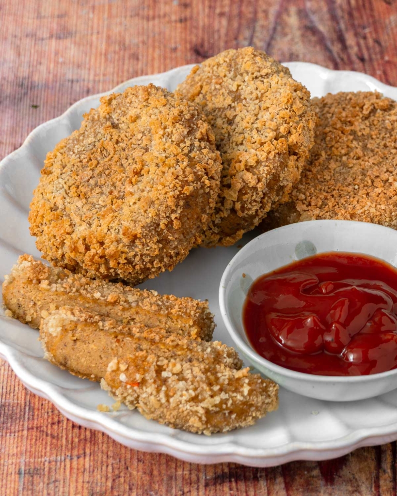 Golden, crispy, breadcrumb coated vegan chicken patties on a place with ketchup in a dish beside