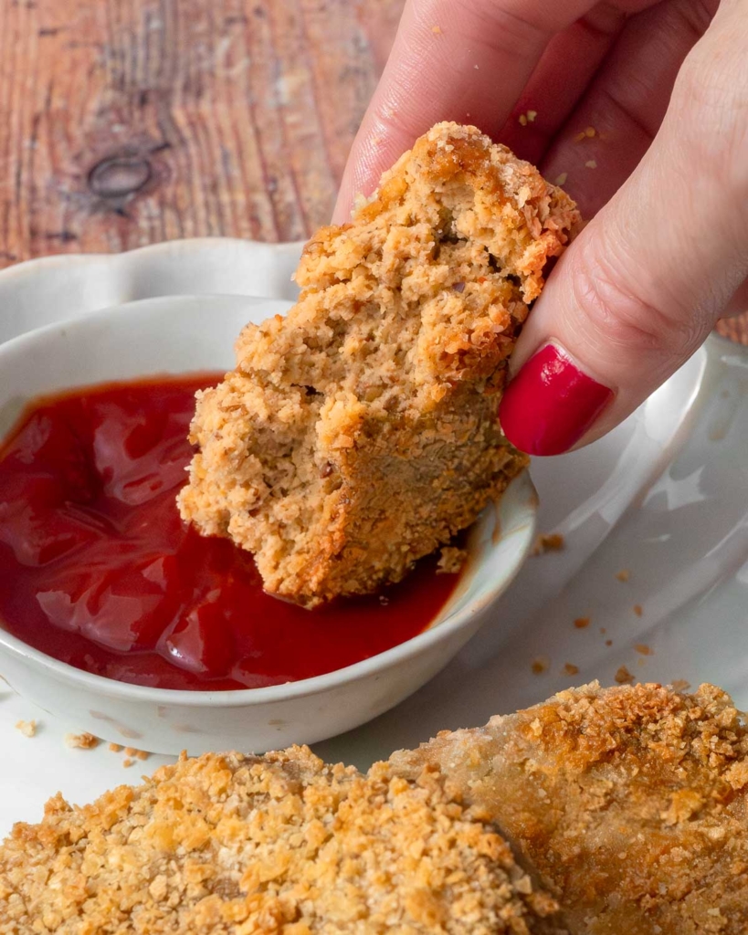 A vegan chicken patty being dipped in ketchup