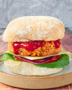 A homemade gluten free vegan chicken burger in a bun with ketchup drizzling down the side