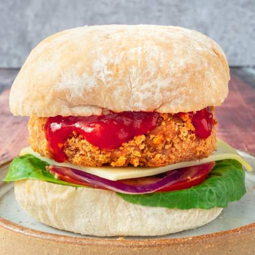 A homemade gluten free vegan chicken burger in a bun with ketchup drizzling down the side