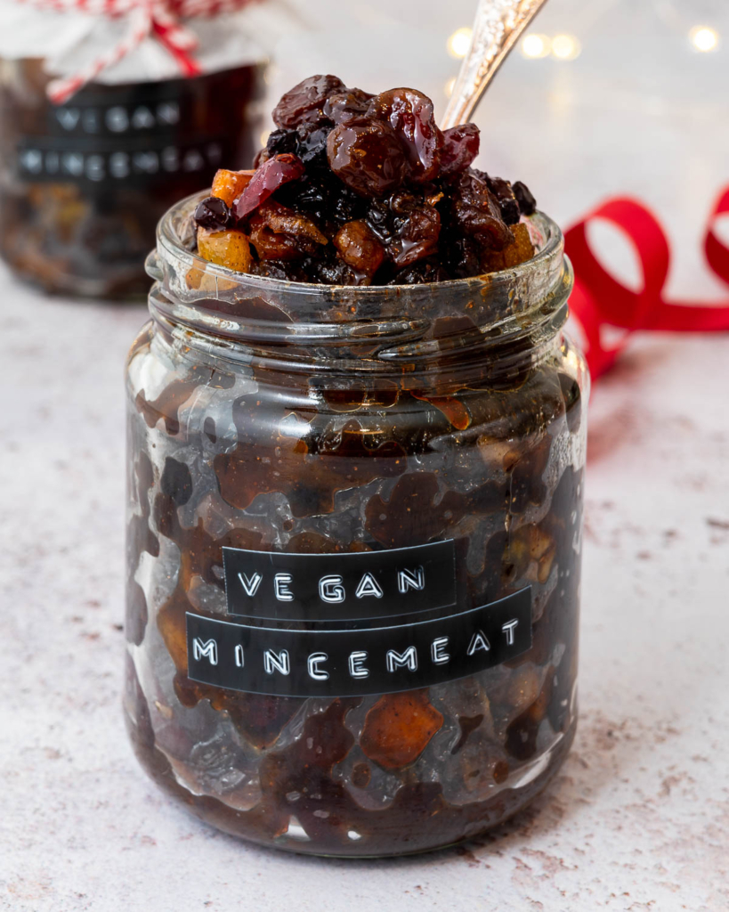 A jar of juicy, fruity, saucy vegan mincemeat without suet, with bokeh Christmas lights and an out of focus red ribbon in the background